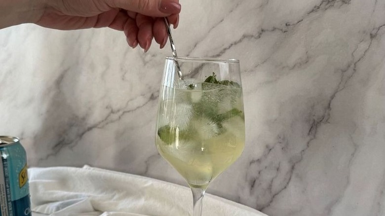 Hand using spoon to stir cocktail in wine glass