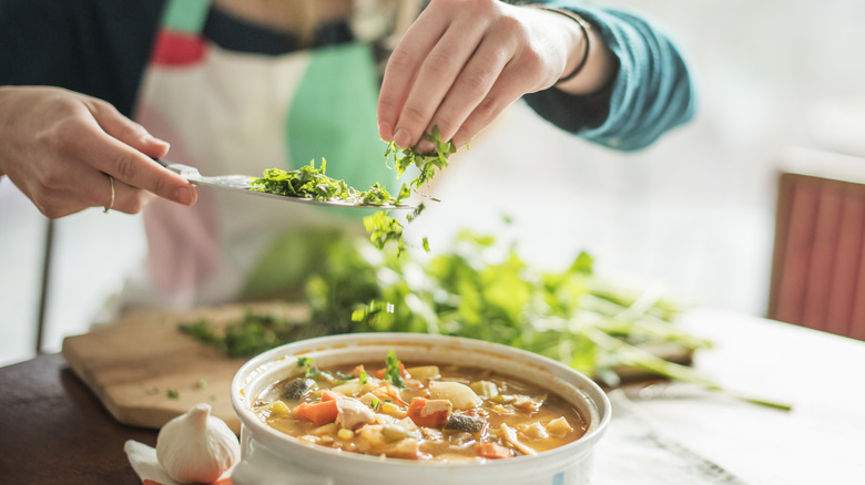 Woman adding chopped green herbs to pot of soup