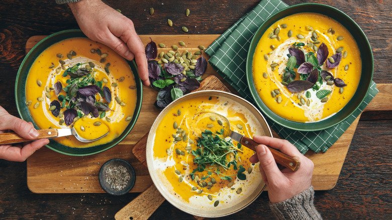 Bowls of creamy pumpkin soup on wooden board