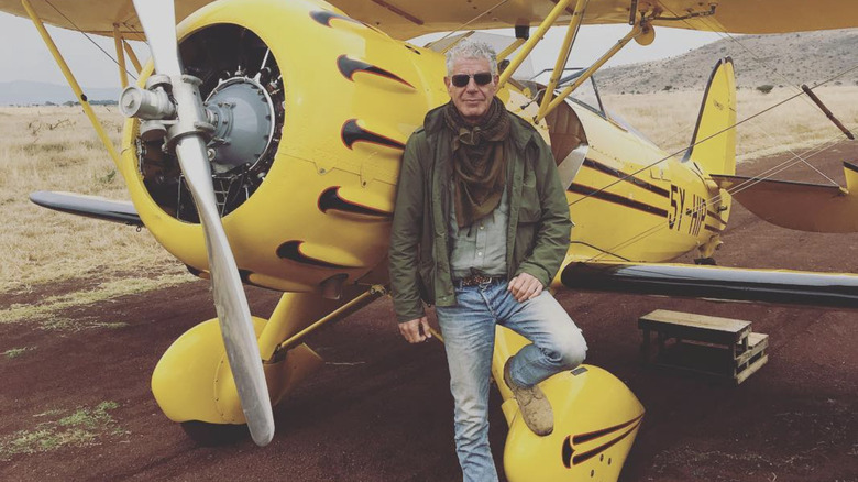 Anthony Bourdain standing outside yellow airplane