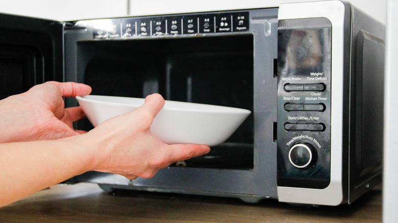 Two hands putting a white ceramic bowl into a microwave