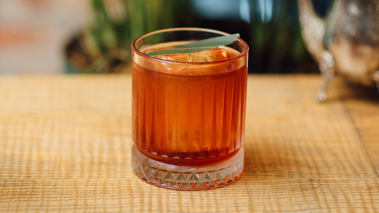 An Oaxacan/mezcal negroni in a classy lined glass with an agave leaf garnish on a yellow table