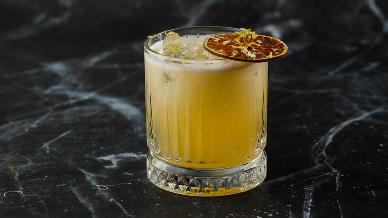 a bright yellow mezcal cocktail in a lined glass and dried orange peel garnish on a black marble tabletop