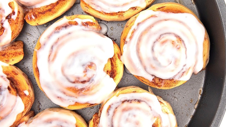 Baked cinnamon rolls with icing in a round metal pan