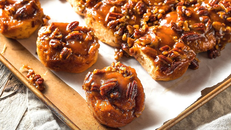 Sticky caramel nut rolls on a lined sheet pan