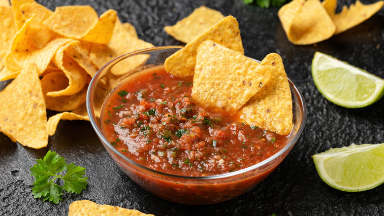 A bowl of salsa with some chips and limes