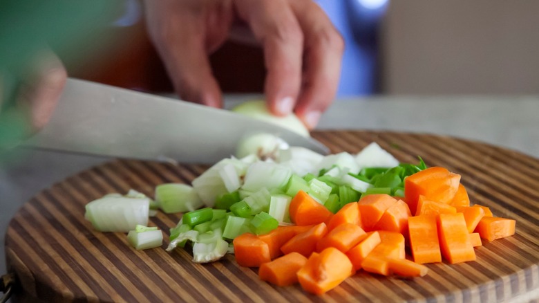 a person cutting mirepoix vegetables, celery, carrots, and onion