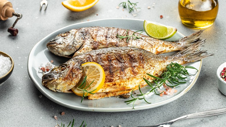 Two whole grilled fish on plate with lemon and rosemary sprigs