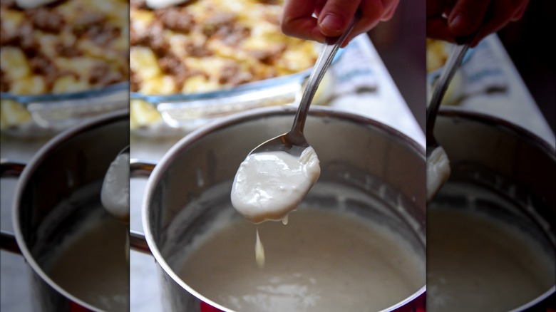 Holding spoonful of homemade béchamel sauce above pot