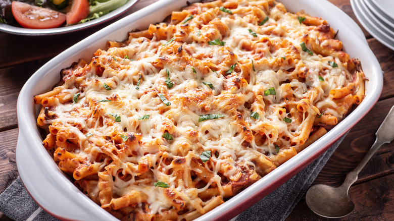 A hot casserole dish of baked ziti, topped with chopped basil