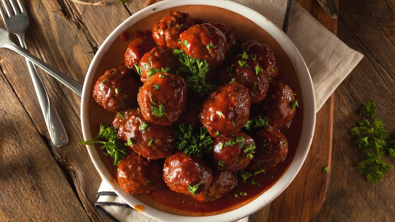 Large white bowl filled with saucy meatballs and chopped parsley