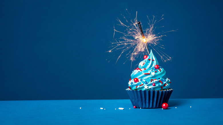 cupcake with blue frosting, red, white, and blue sprinkles, and a sparkler