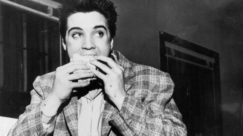 Black and white photograph of Elvis Presley eating a sandwich