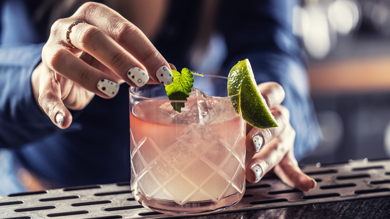 Margarita cocktail being decorated with mint leaf