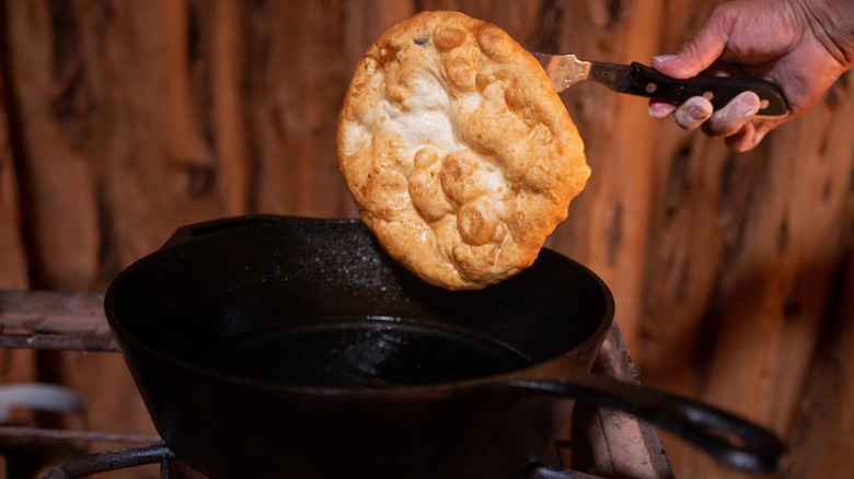 Fry bread being pulled from the oil in a cast iron skillet