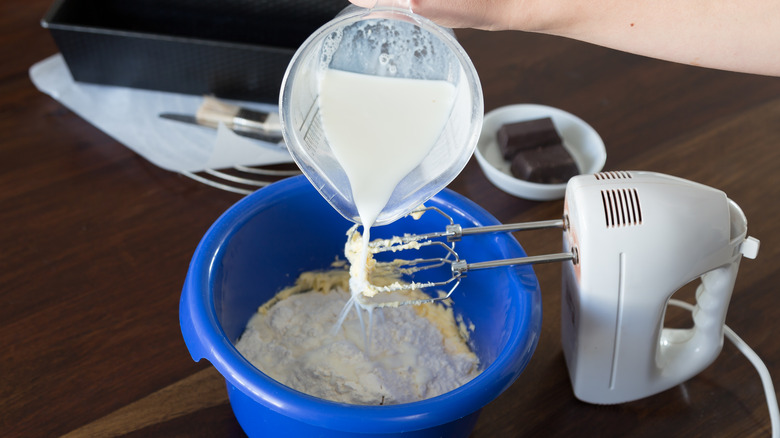 adding milk to cake batter with hand mixer