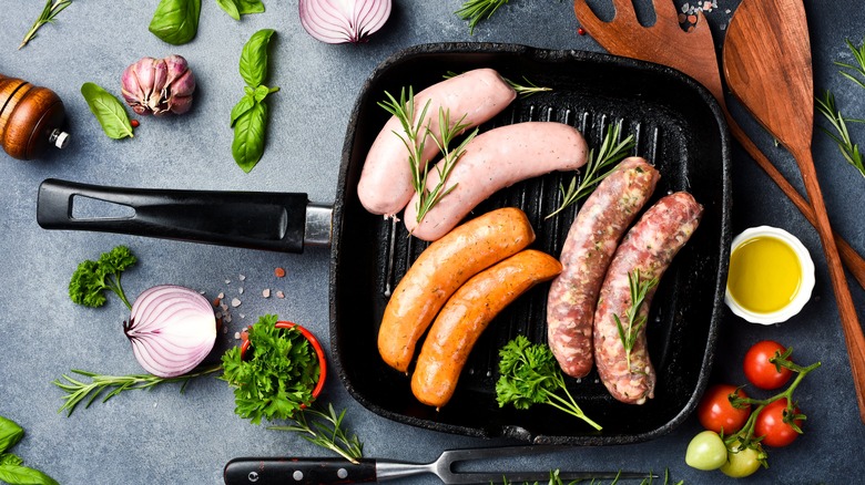 Pan with various raw sausages surrounded by herbs and veggies