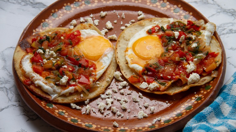 A pair of huevos rancheros on a ceramic brown plate