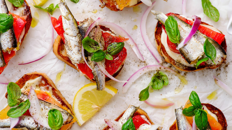 Crostini topped with sardines, basil, and tomatoes