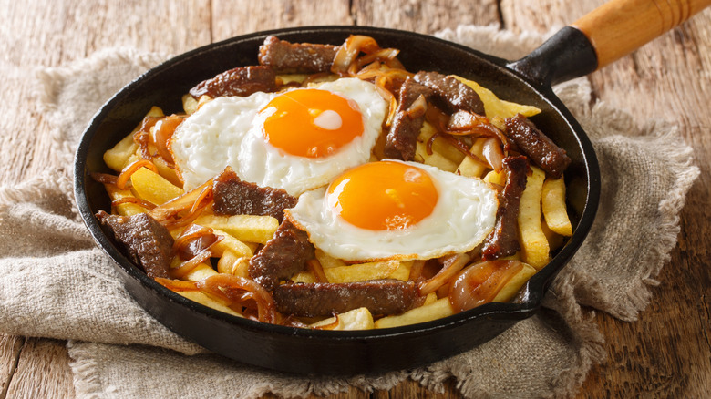 French fries with fried eggs and strips of steak in a cast iron skillet