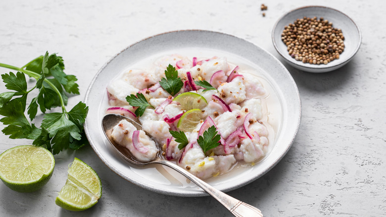 fish ceviche on white plate with fresh herbs and lime