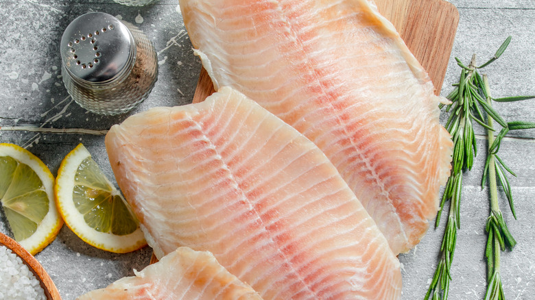 cutlets of raw white fish next to lemon slices and rosemary