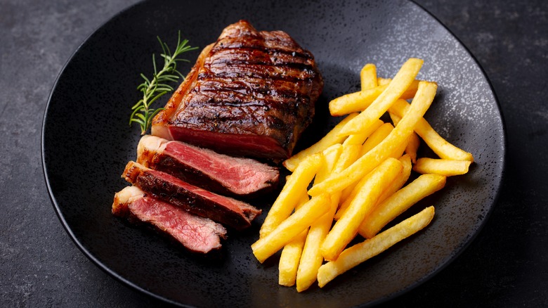 Grilled sliced steak with french fries on a black plate