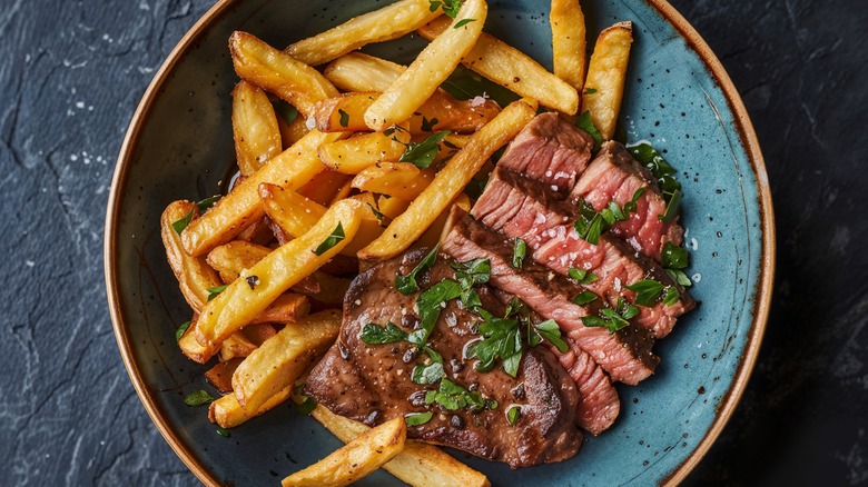 Sliced steak with fresh herbs next to french fries on blue plate