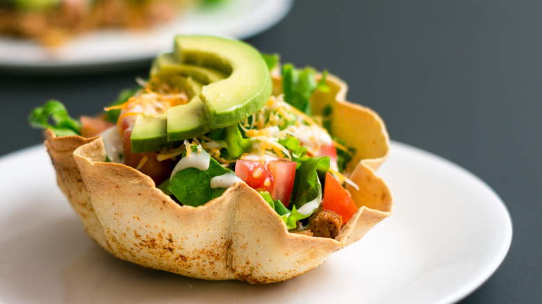 A taco salad in a crisp, edible tortilla bowl sits on a white plate