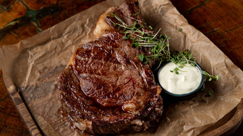 A juicy steak clearly has a golden crust and sits next to garlic cream sauce