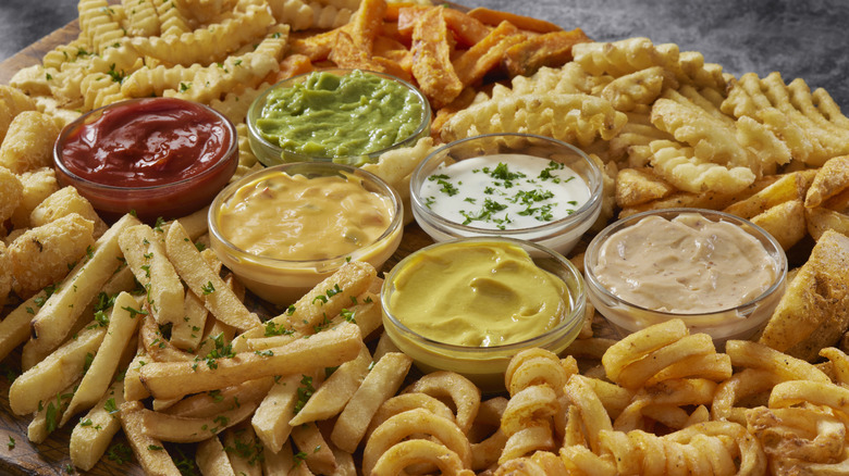 Assortment of different french fries surrounded by bowls of various dipping sauces