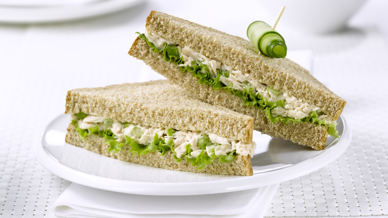 A tuna sandwich with lettuce on whole-wheat bread, cut into two triangles, layered on a white plate