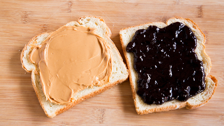 Two slices of bread — one with peanut butter and the other with jelly — sit next to each other on a wooden surface.