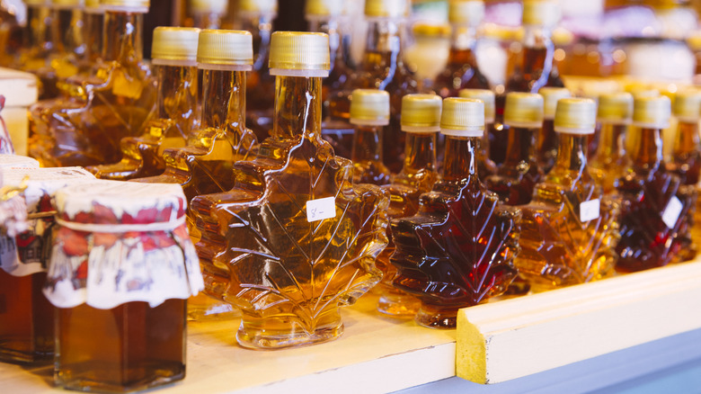 Rows of maple syrup bottles, some shaped like maple leaves, in different color grades