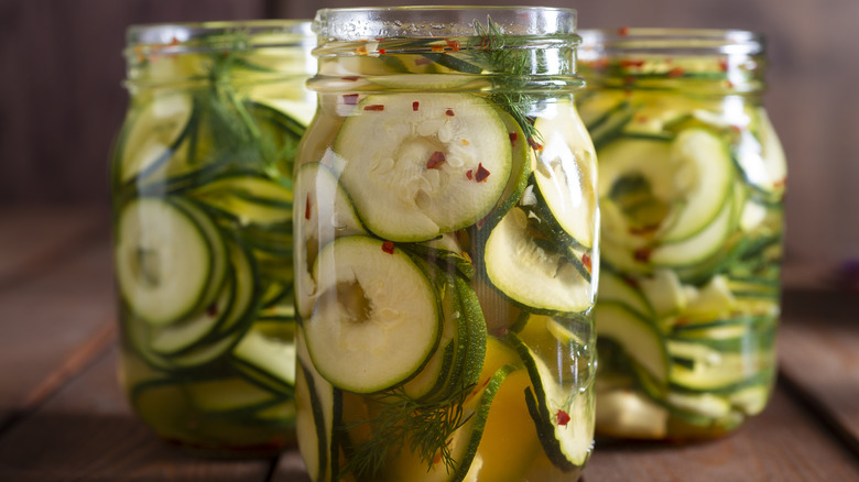 Sliced cucumbers float in spiced brine inside glass jars