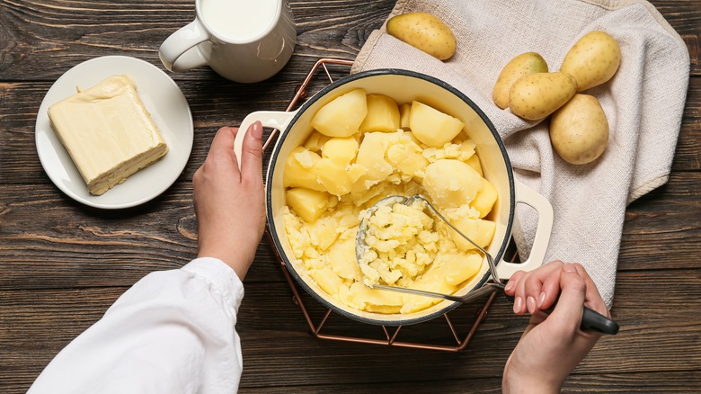 Hands mashing potatoes in pot