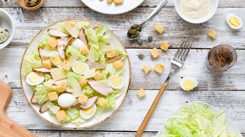 Caesar salad with chicken and eggs next to capers