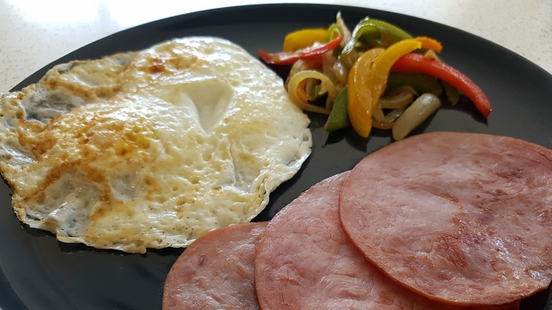 over easy egg, ham, and fried peppers on black plate