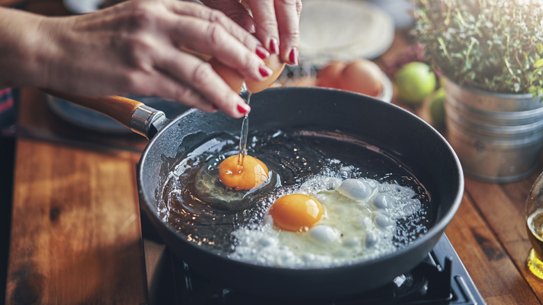 woman breaking egg into frying pan