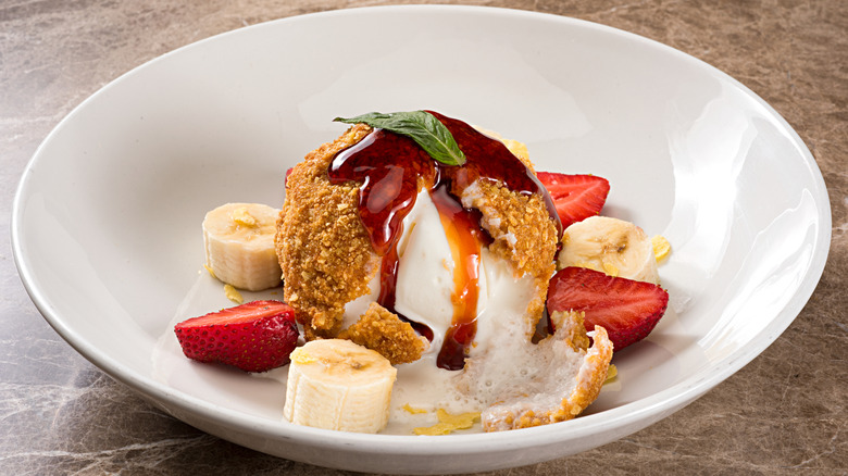 A fried ice cream ball with strawberries and bananas and a drizzle of fruit syrup and a basil leaf