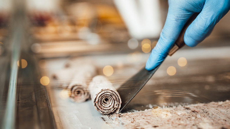 A gloved hand rolls a strip of stir-fried ice cream