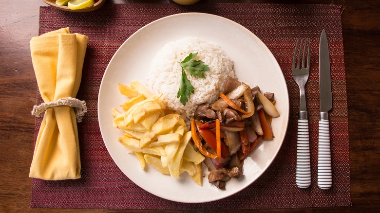 Plate of lomo saltado on white plate next to cutlery