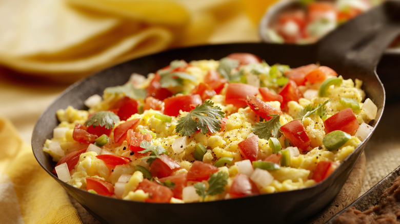 Scrambled eggs with tomatoes and chiles in black skillet