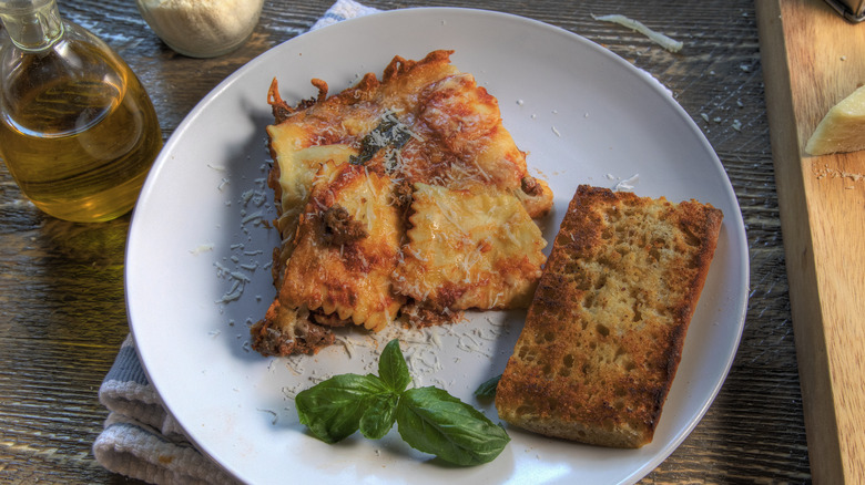 Baked ravioli lasagna slice with garlic bread on white plate