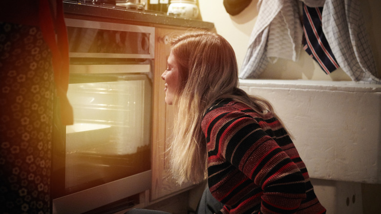 A woman looks inside an oven with the light on.