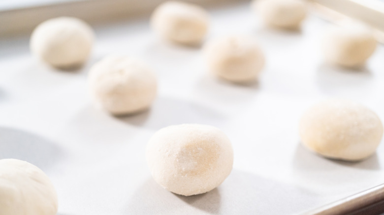 Rising frozen dinner rolls rest on a baking sheet.