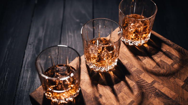 Three glasses of bourbon on a wooden table in a dimly lit room with shadow cast behind each glass