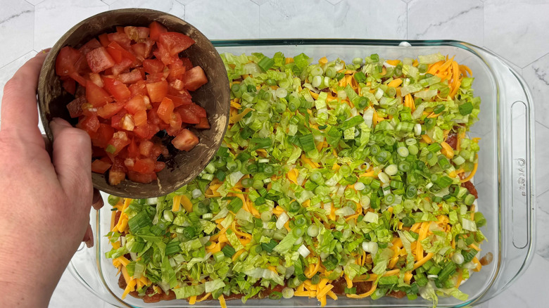 Bowl of diced tomatoes over taco dip in large dish