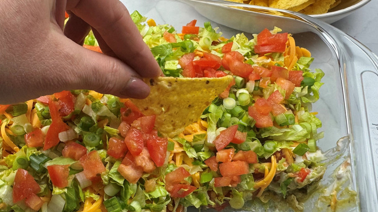 Hand dipping tortilla chip into taco dip