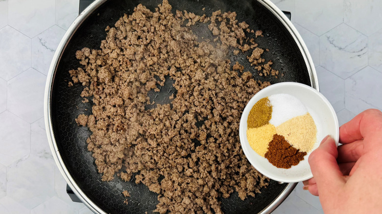 Bowl of seasonings over ground beef in skillet